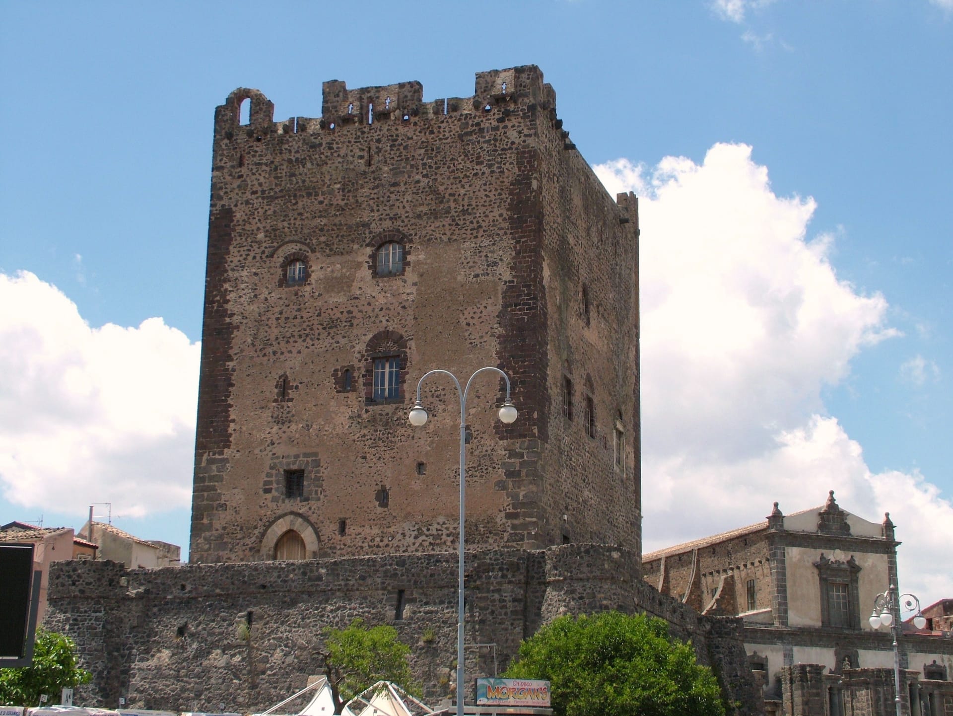 La torre del castello normanno di Adrano in pietra lavica sotto un cielo con nuvole