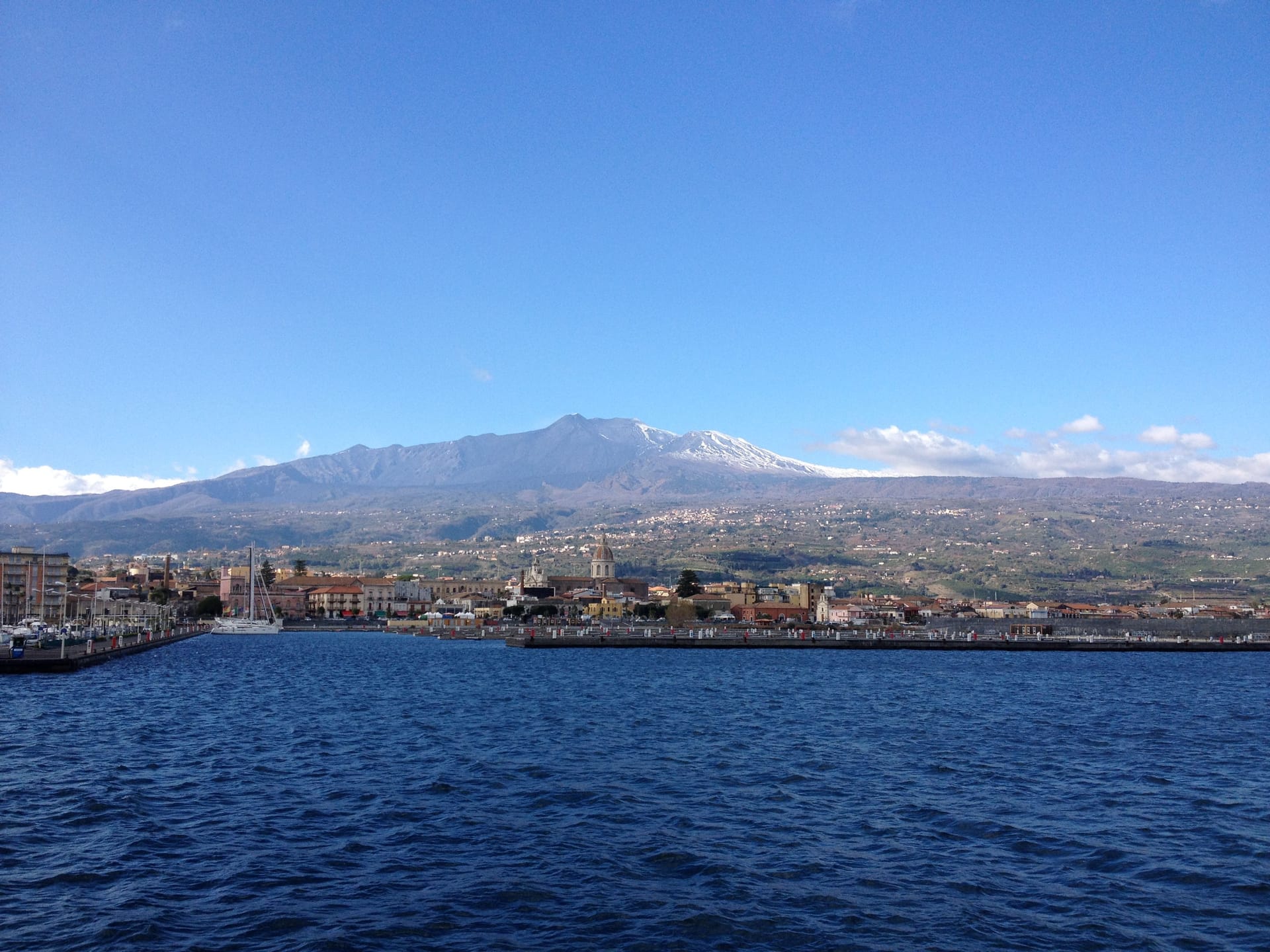 Il porto di Riposto visto dal mare, con la costa e l'Etna innevato sullo sfondo