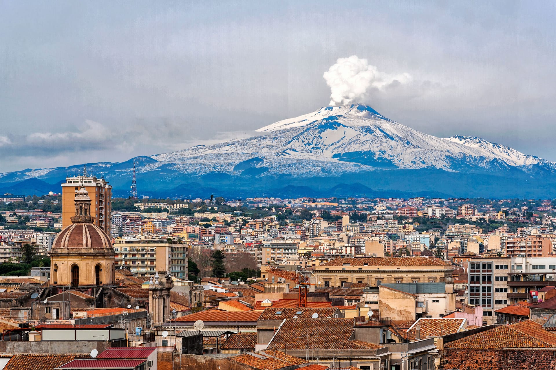 Skyline di Catania dall'alto con i tetti della citta' e l'Etna innevato con il pennacchio di fumo sullo sfondo